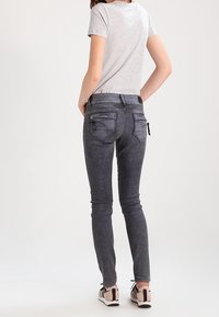 Jeans ajustados grises con una textura suave, con bolsillos traseros con cremallera y una cintura de altura media. Combinados con una camiseta gris y zapatos casuales.