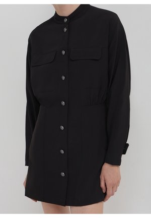 Schwarzes Langarm-Minikleid mit Stehkragen, vorderen Klapptaschen und einer Reihe silberner Knöpfe in der Mitte.