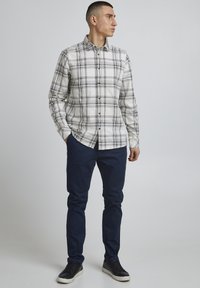 Rutete langermet skjorte i hvit og svart, paret med marineblå chinos og sorte joggesko. Skjorten har krage med knapp og vanlig passform.