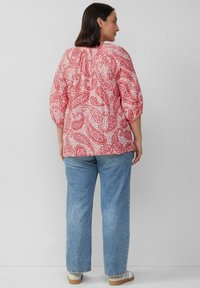 Rood en wit paisleypatroon blouse met ballonmouwen, relaxte pasvorm en geplooide halslijn, gecombineerd met lichtblauwe rechte jeans.