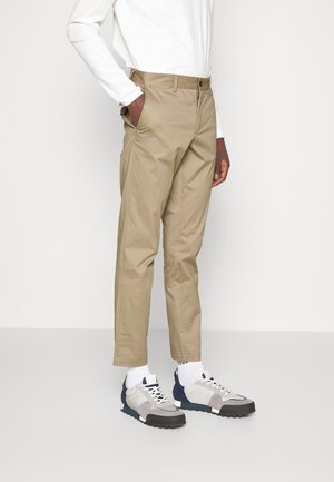 Pantalons kaki à coupe droite, fabriqués en coton, dotés de poches latérales, d'une taille avec passants de ceinture, et associés à des baskets grises et bleues.