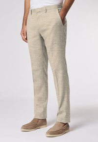 Beige Leinenmischungshosen mit strukturierter Oberfläche, slim fit, seitlichen Taschen und flachem Vorderdesign. Getragen mit hellbraunen Slippers.