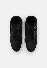 Černé semišové vysoké boty s odpovídajícími tkaničkami, kovovými očky a bílou gumovou podešví. Vyznačují se hladkým povrchem a bočním zipovým uzávěrem.