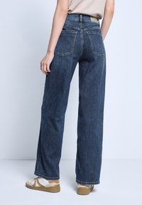 Jeans de pierna ancha de lavado oscuro, fabricados en denim, con una cintura alta, dos bolsillos traseros y un dobladillo limpio. Combinados con zapatillas deportivas ligeras.