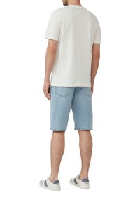 T-shirt blanc à manches courtes pour homme associé à un short en denim bleu clair, mettant en avant une coupe décontractée et un design casual. Baskets blanches avec des accents gris.
