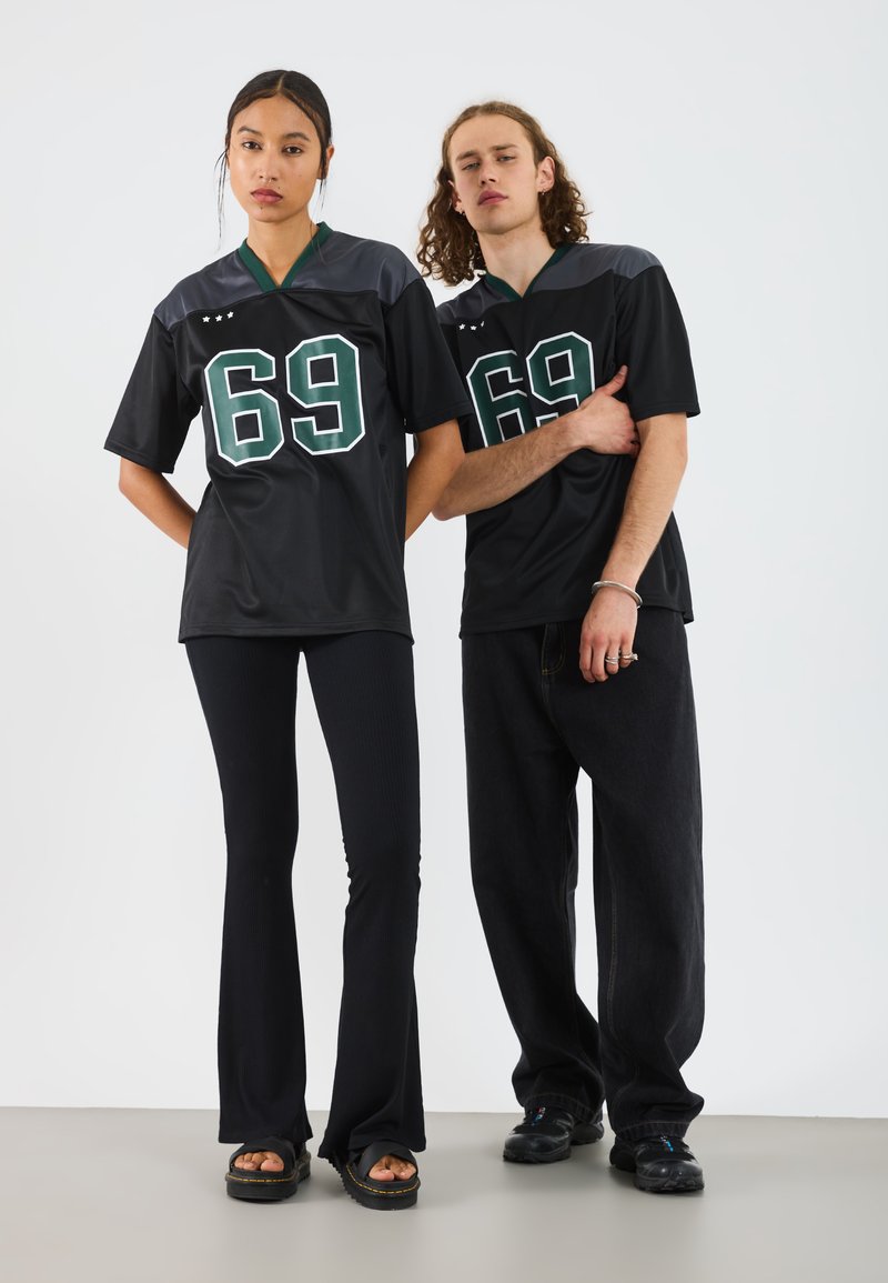Jersey deportivo negro con el número verde "69", combinado con unos pantalones de campana negros con textura. La modelo lleva sandalias negras gruesas. Diseño minimalista.