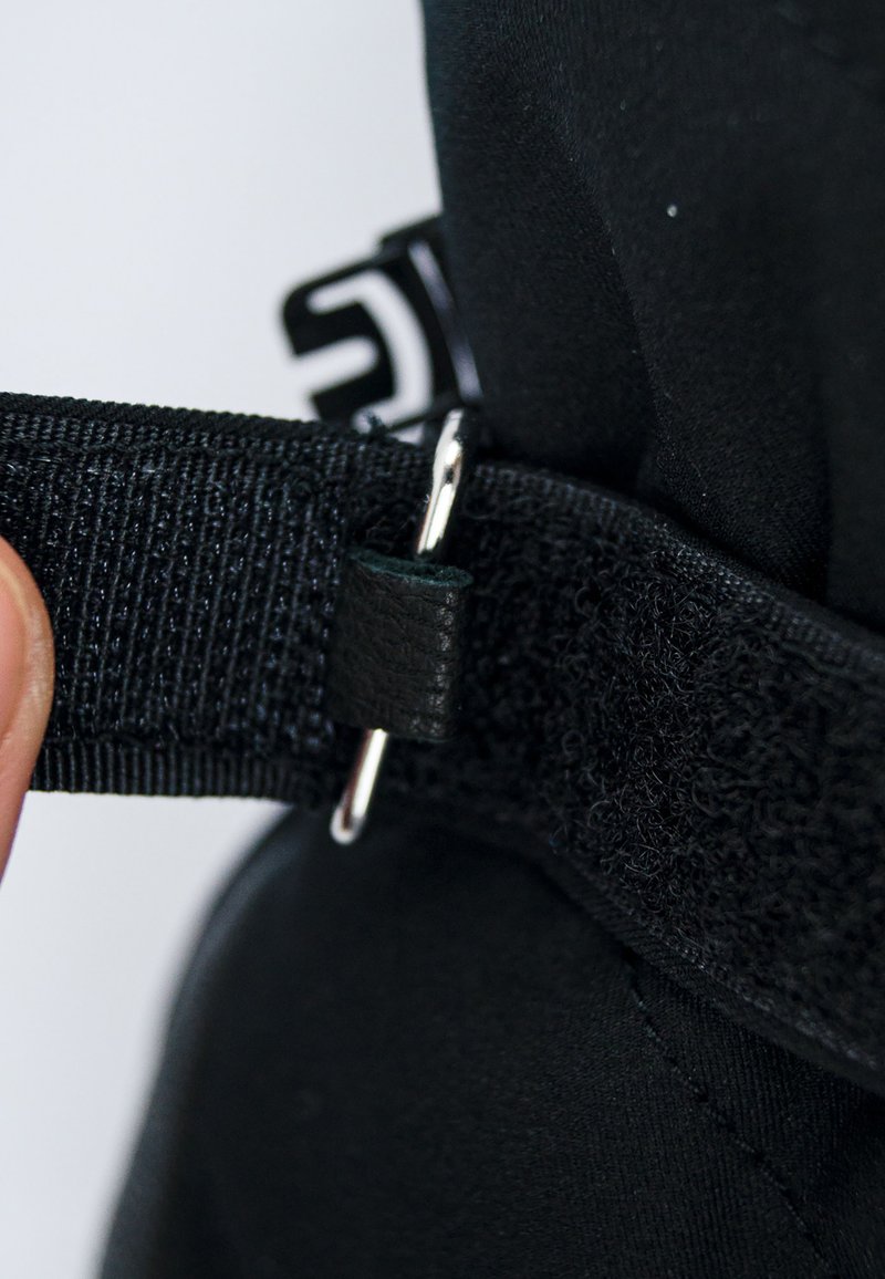 Cinturino in tessuto nero con superficie texturizzata, dotato di un anello in metallo argentato e di un piccolo dettaglio in pelle nera. Inquadratura ravvicinata della chiusura.