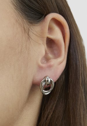Ohrringe aus silberfarbenem Metall mit ineinandergreifenden kreisförmigen Formen, glatter Textur und polierter Oberfläche, getragen am Ohrläppchen.