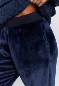 Pantaloni jogger blu navy realizzati in tessuto morbido, con vita a coste e una consistenza liscia con un leggero lucido.