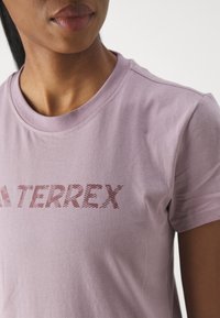 Světle fialové bavlněné tričko s kulatým výstřihem a texturovaným grafickým potiskem ve tmavším odstínu, na kterém je na hrudi nápis "TERREX".
