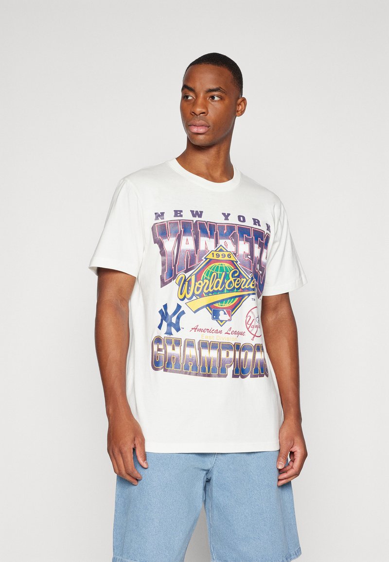 Balta medvilninė marškinė su spalvinga grafika, kurioje užrašyta "NEW YORK YANKEES 1996 METŲ PASAULIO ČEMPIONATAS" ir beisbolo motyvais.