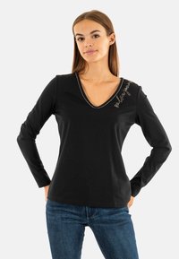 Maglietta nera a maniche lunghe con scollatura a V, caratterizzata da un accento argento sul colletto e testo ricamato sulla spalla sinistra. Materiale in cotone morbido.