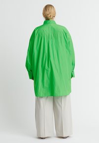 Groene oversized shirt van lichte stof, met een hoge kraag en knoopmanchetten, gecombineerd met losse beige broek.