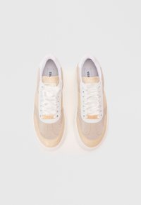 Un paio di sneaker beige e bianche con lacci in satin e etichetta del marchio metallica su uno sfondo chiaro.