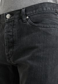 Black denim jeans with a smooth texture, a silver button closure, and standard pockets. The fabric features subtle fading and a classic cut.