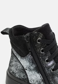 Svarte og sølv ankelsko med glitrende tekstur, glidelås på siden, semsket aksenter og svarte snøring, med forsterket hæltab.