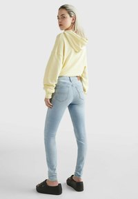 Sudadera de gran tamaño en amarillo claro combinada con jeans ajustados de cintura alta en azul claro, que cuentan con bolsillos traseros, llevada con sandalias de plataforma negras.