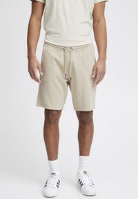 Shorts de survêtement beiges en tissu doux, avec une ceinture élastique à cordon de serrage, poches latérales et une coupe décontractée.