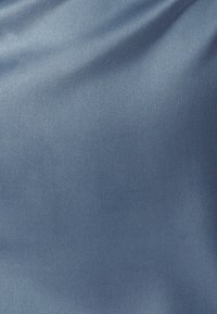 Siidist kangas helesinises toonis, pehme tekstuuriga. Materjal peegeldab valgust, luues õrnu, peeneid lainetusi ja variatsioone.