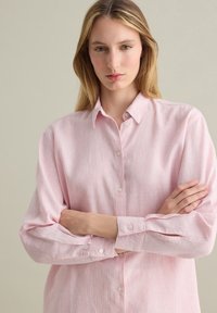 Light pink, striped button-up shirt with a collar, long sleeves, and button cuffs. Smooth texture with an even pattern throughout.