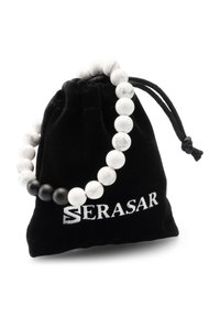 Black velvet pouch with a drawstring, featuring a white marble bead bracelet with alternating black beads and a branded logo in silver.