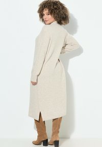 Maglione lungo beige a maglia con alta scollatura, maniche a coste e spacchi laterali, abbinato a stivali in suede tan al ginocchio.