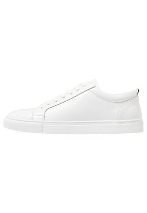 Weißer flacher Leder-Sneaker mit weißen Schnürsenkeln, flacher Sohle und Zuglasche hinten, von der Außenseite gezeigt.