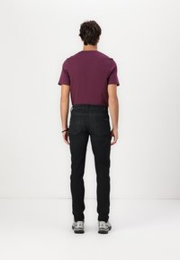 Fialové tričko s krátkým rukávem a černé slim-fit džíny. Hladká látka, standardní kulatý výstřih, s kapsami na zadní straně džín. Šedé tenisky.