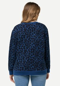 Granatowy sweter z leopardzim wzorem w ciemniejszym odcieniu niebieskiego, z prążkowanymi mankietami i dołem, o luźnym kroju i miękkiej fakturze.