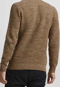 Pull en tricot marron avec une finition texturée, des poignets et un ourlet côtelés, et un col rond. Des coutures visibles ajoutent des détails au design.