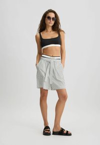 Crni crop top s bijelim rubovima, prugaste bijele i crne kratke hlače s remenom na vezanje i crne sandale. Dodaci uključuju velike sunčane naočale.