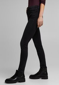 Jeans negros ajustados con una textura suave, cintura alta, costuras visibles y un ajuste ceñido. Combinados con botines negros que presentan acentos texturizados.