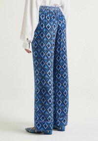 Pantaloni a gamba larga con motivo a diamante blu. Presentano una fascia elastica in vita e una texture del tessuto liscia. Abbinati a calzature coordinati.