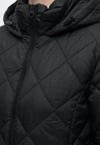 Veste matelassée noire avec col montant, fermeture éclair devant et cordon réglable à la capuche.