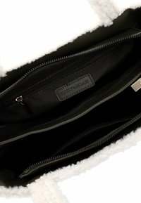 Borsa tote esterna in shearling bianco con fodera interna scura, caratterizzata da una tasca con zip e un'etichetta impresso "EMILY & NOAH". Manici robusti.