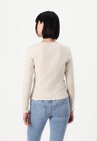 Lys beige strikkegenser med lange ermer, ribbestruktur, subtil bølgekant, brukt sammen med lyseblå tettsittende jeans.