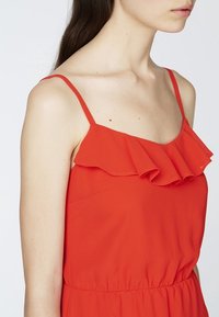 Rotes ärmelloses Kleid mit Rüschensaum, aus leichtem Stoff gefertigt. Verfügt über dünne Spaghetti-Träger und einen elastischen Bund.