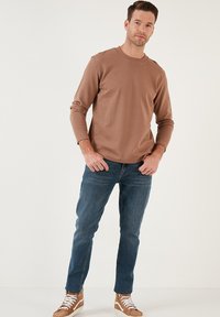 Pruun pikade varrukatega särk, millel on ribakujuline tekstuur, koos siniste teksadega. Sneakerid on valmistatud tan ja valgete toonide kombinatsioonist.