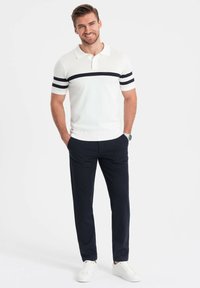 Polo shirt in het wit met marineblauwe strepen, kortemouwen en een kraag, gecombineerd met slim-fit donkerblauwe broek en witte sneakers.