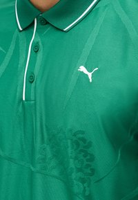 Πράσινο πόλο με διακριτικά σχέδια φύλλων, λευκό λογότυπο Puma στο στήθος και τρία πράσινα κουμπιά κάτω από τον γιακά.