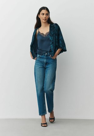 Dark blue floral-patterned kimono over a dark satin camisole, paired with light blue high-waisted jeans and black open-toe sandals.