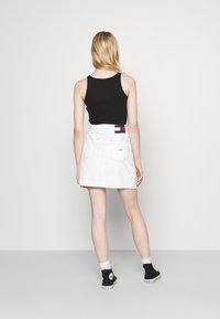 Gonna in denim bianco a vita alta, con tasche posteriori e un'etichetta con marchio. Indossata con una canotta nera e sneakers nere alte.