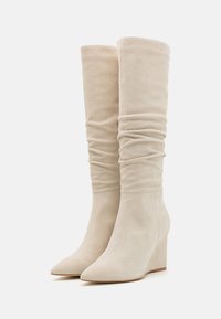 Bottes à talons compensés beige en daim doux, avec un design flou, un bout pointu et une finition texturée. Idéales pour un look à la fois élégant et confortable.