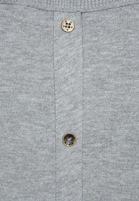 Tessuto a maglia grigio con una patta di bottoni che presenta due bottoni circolari in tonalità oro. La texture sembra morbida e leggermente elastica.