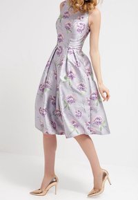 Laventeli satiinista valmistettu kukkakuosiset mekko, jossa on istuva yläosa, levenevä helma ja hienovarainen kiilto. Ominaisuudet violetteja ja vihreitä kukkakuvioita.