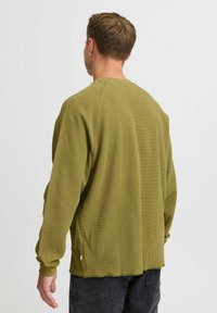 Căma�șă lungă cu mâneci verzi măslinii, dintr-un material texturat, cu o croială lejeră, guler cu nervuri și slituri laterale la tiv.