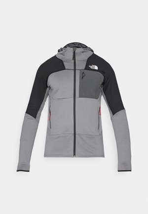 Veste zippée gris et noir avec capuche ; présente un tissu texturé, des panneaux en mesh, deux poches latérales et un logo sur le haut à gauche de la poitrine.