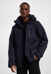 Tamsiai mėlyna šilta striukė su gobtuvu, keliais kišenėmis ir užtrauktuku priekyje. Sukurta su lygiu paviršiumi ir reguliuojamais rankogaliais.