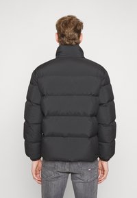 Černá péřová bunda s vysokým límcem, prošívaným vzorem, elastickými manžetami a hladkou texturou. Navržena pro teplo a pohodlí.