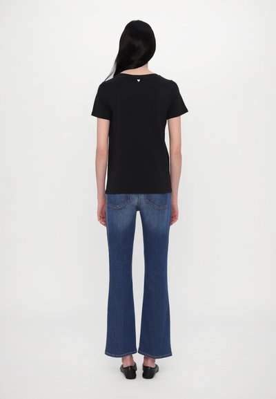 Sort bomulds t-shirt med korte ærmer, rygdetalje med et lille logo. Båret med flagrende blå denim jeans og sorte sko.